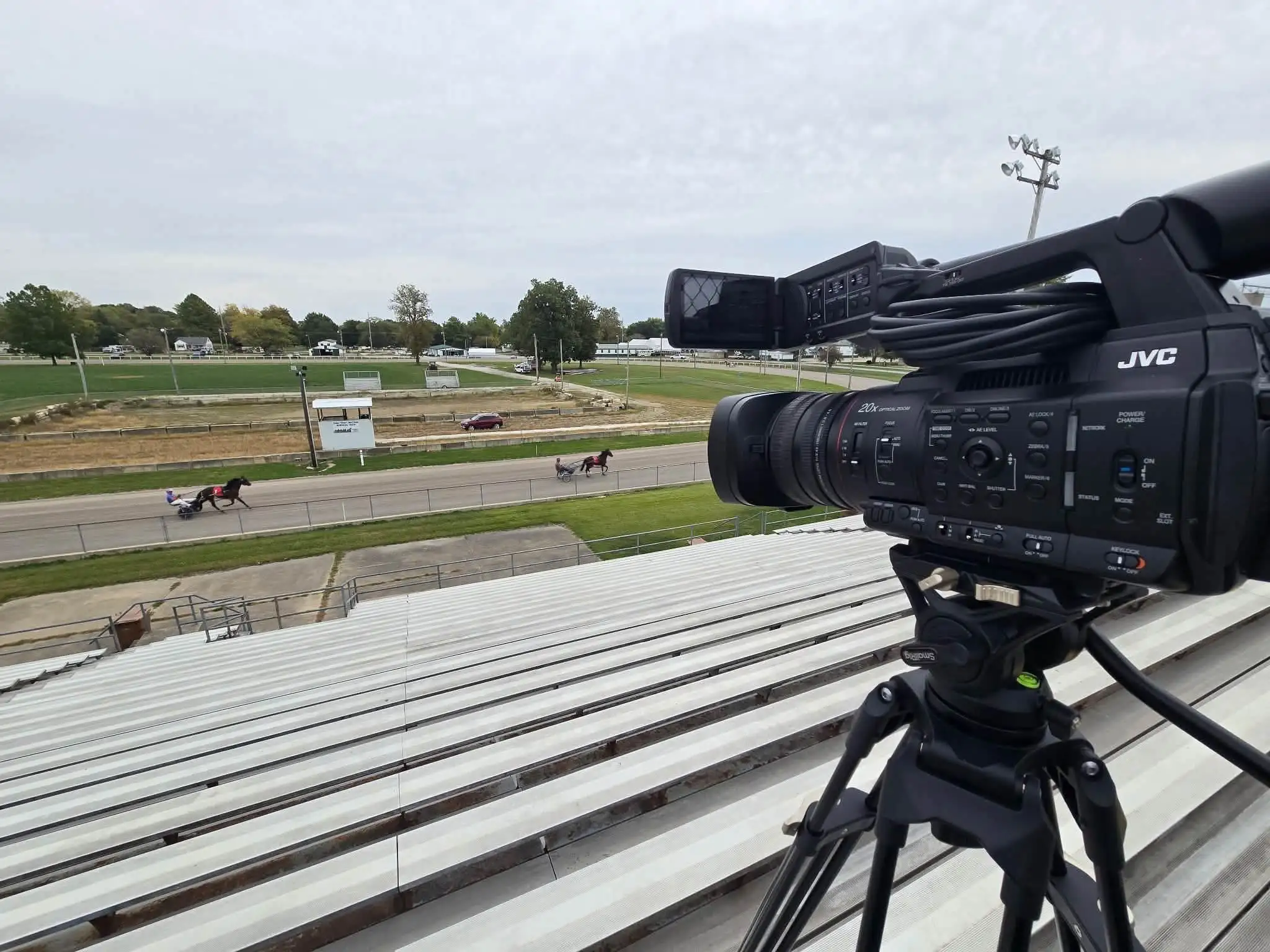 A camera on a tripod at a dirt racetrack, aimed at the cars on the track